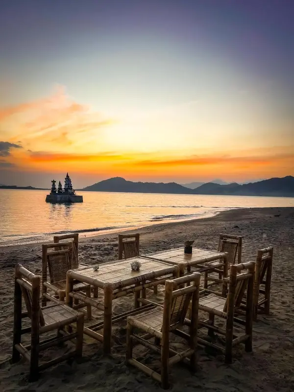 Tables et chaises en bois disposées sur une plage au coucher du soleil.