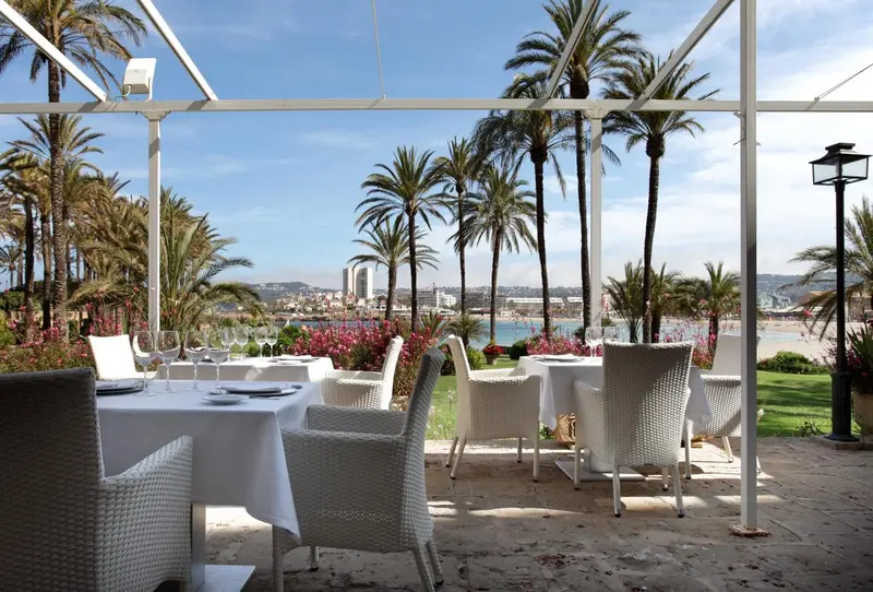 Tables dressées en terrasse avec vue sur la mer et la végétation.