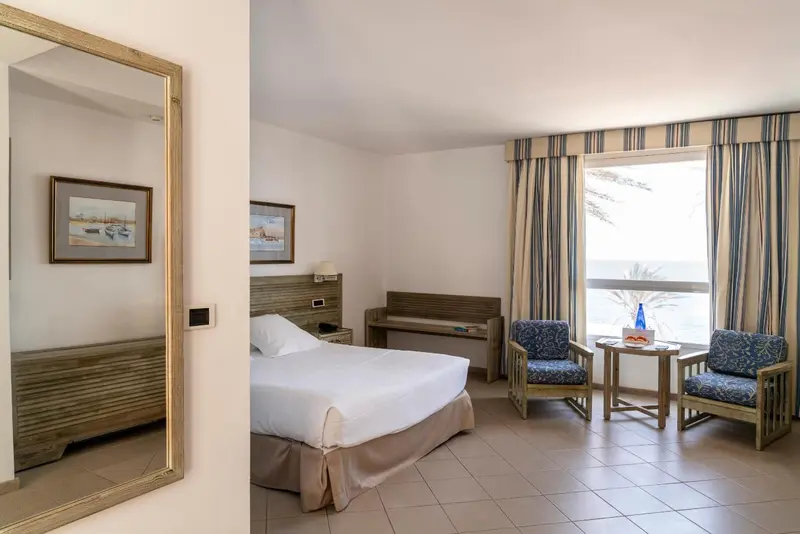 Une chambre lumineuse avec un lit, des fauteuils et une vue sur la mer.