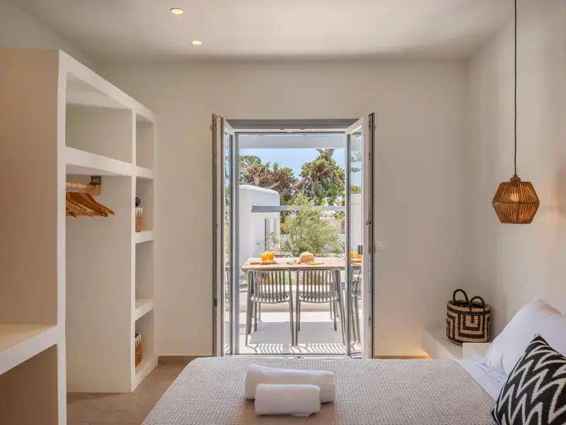 Une chambre lumineuse s'ouvre sur une terrasse avec table et chaises.