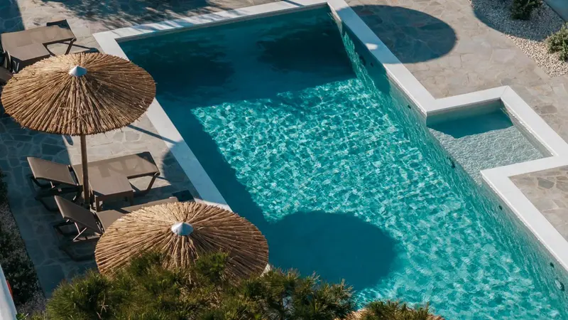 Une piscine rectangulaire bordée de chaises longues et ombragée de parasols en chaume.