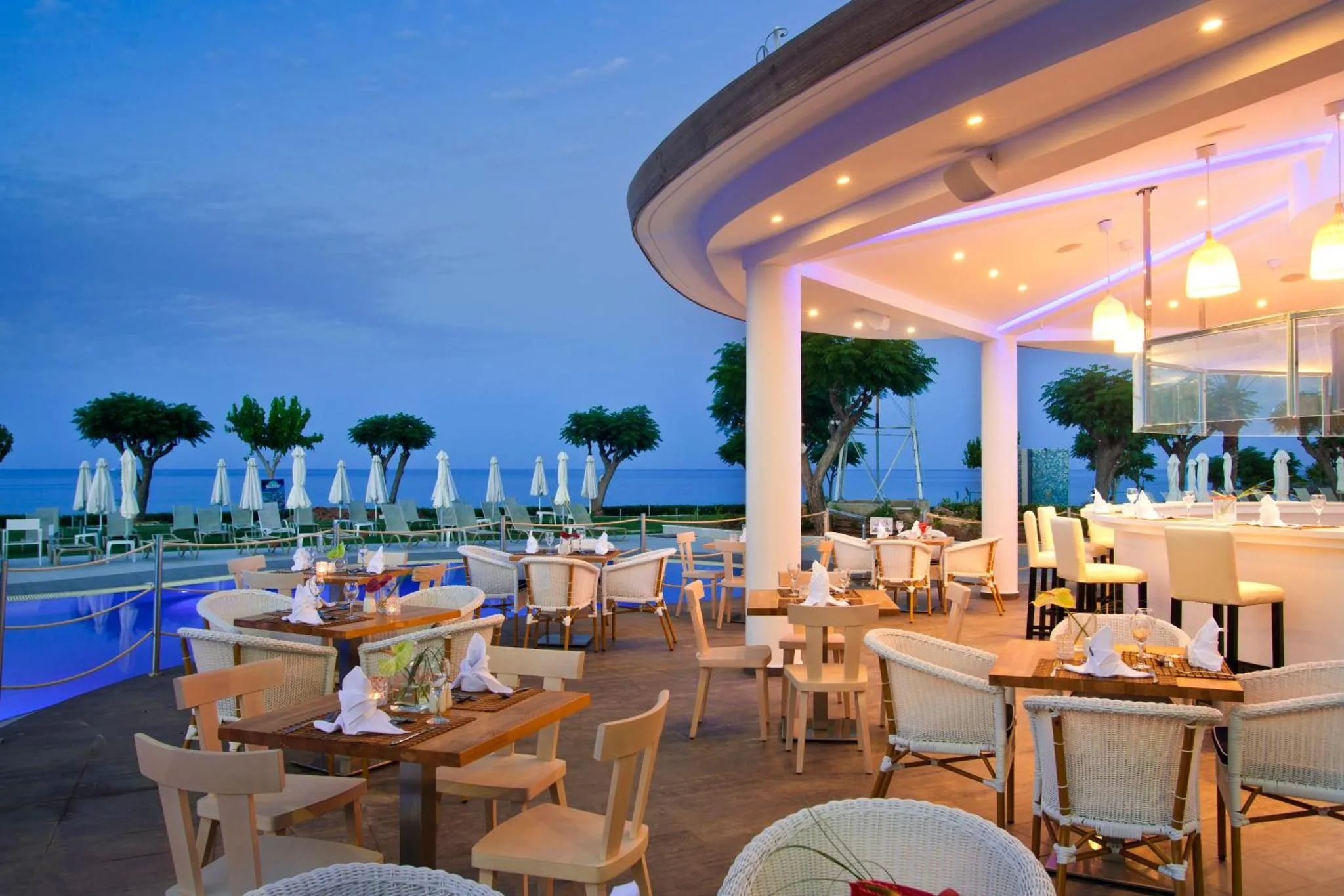 Terrasse de restaurant avec tables dressées face à la mer au crépuscule.