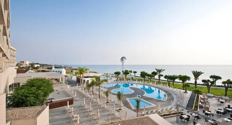 Vue aérienne sur une piscine d'hôtel bordée de palmiers et donnant sur la mer.