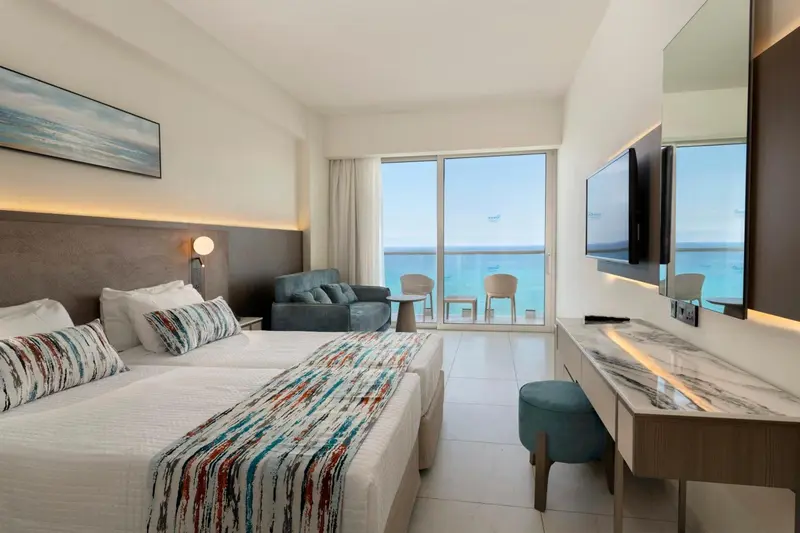 Chambre lumineuse avec un lit double et une vue sur la mer depuis un balcon.