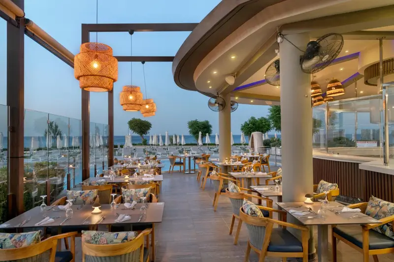 Terrasse de restaurant avec tables dressées et vue sur la mer.