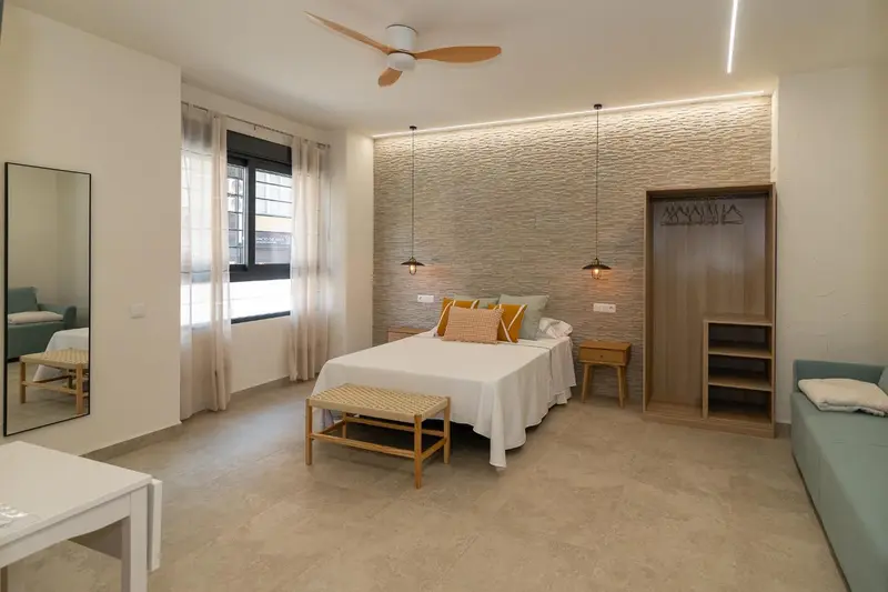 Une chambre lumineuse avec un grand lit et un banc au pied du lit.