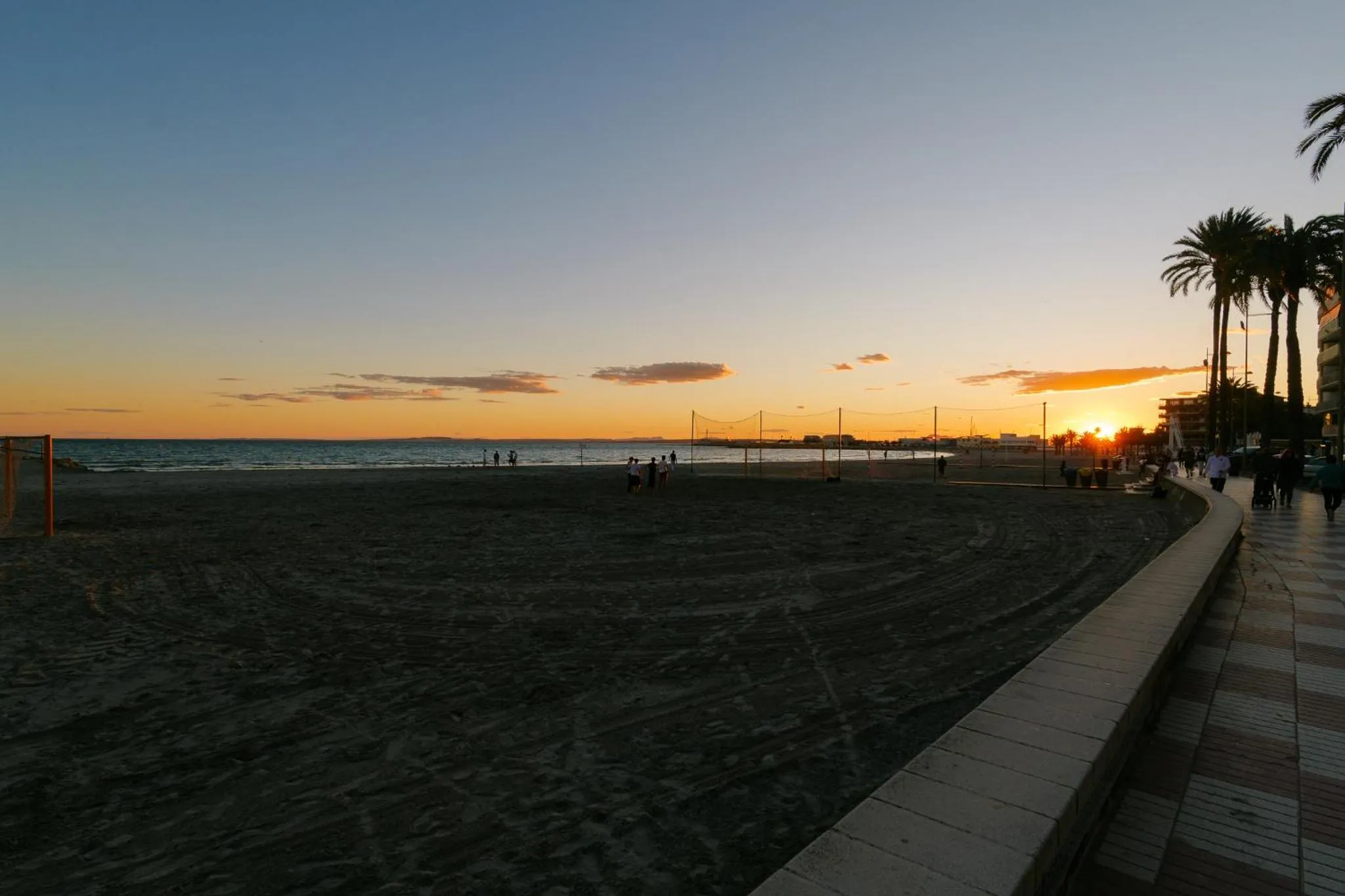 Plage de sable au coucher du soleil avec quelques personnes se promenant.