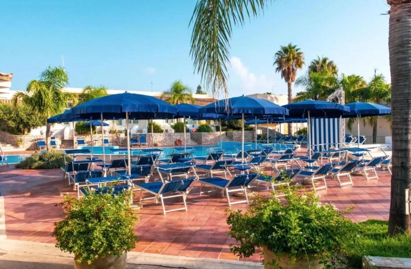Transats bleus disposés autour d'une piscine ensoleillée sous des parasols.