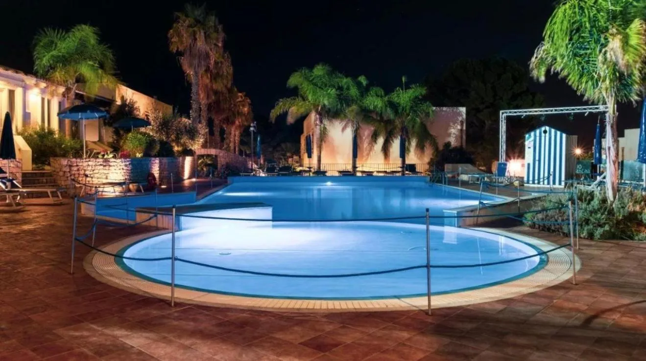 Piscine illuminée au cœur d'un complexe hôtelier tropical la nuit.