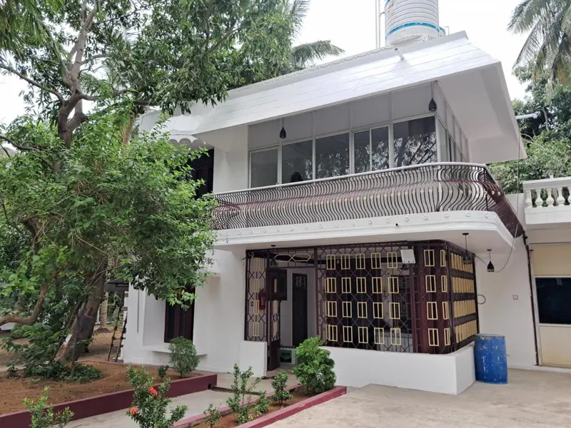 Bâtiment blanc à deux étages avec balcon en fer forgé et végétation luxuriante.