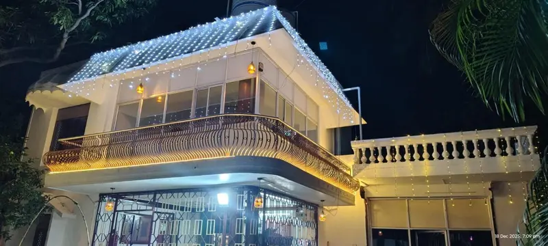 Façade d'un bâtiment illuminée de guirlandes lumineuses et ornée de palmiers.