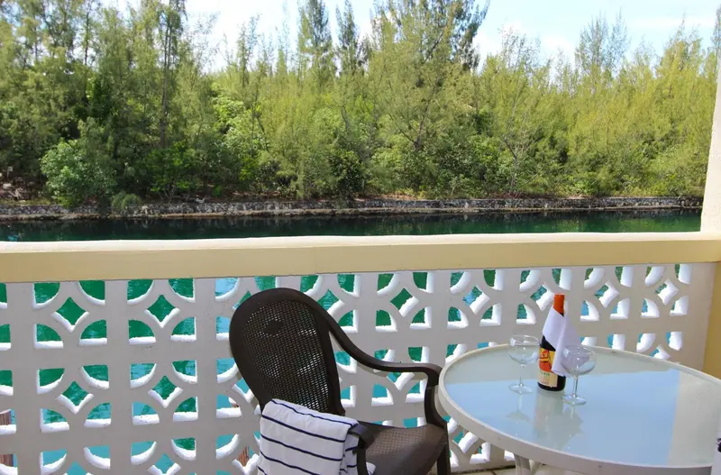 Une terrasse avec une table et des chaises offre une vue sur la végétation et l'eau turquoise.