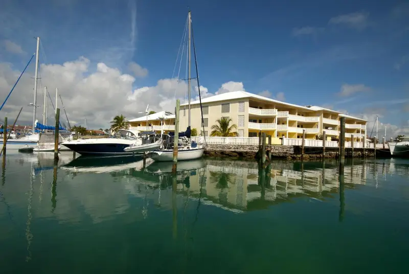 Bâtiment blanc au bord d'une marina ensoleillée, avec des bateaux à quai.
