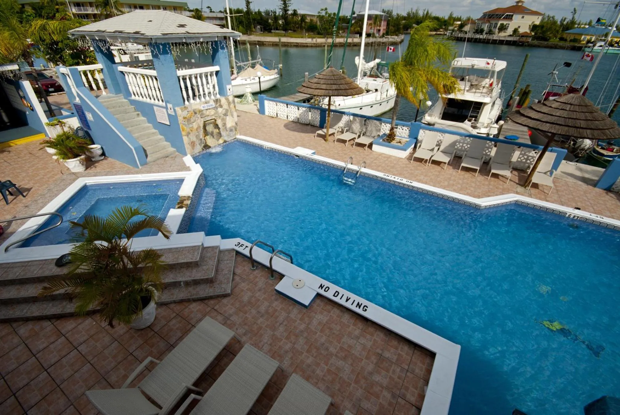Piscine bleue entourée d'une terrasse avec des chaises longues et des parasols.