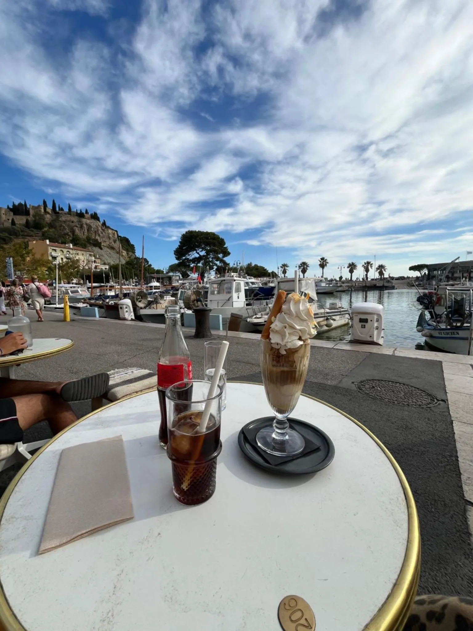 Une table en terrasse présente deux boissons rafraîchissantes avec une vue sur un port de plaisance.