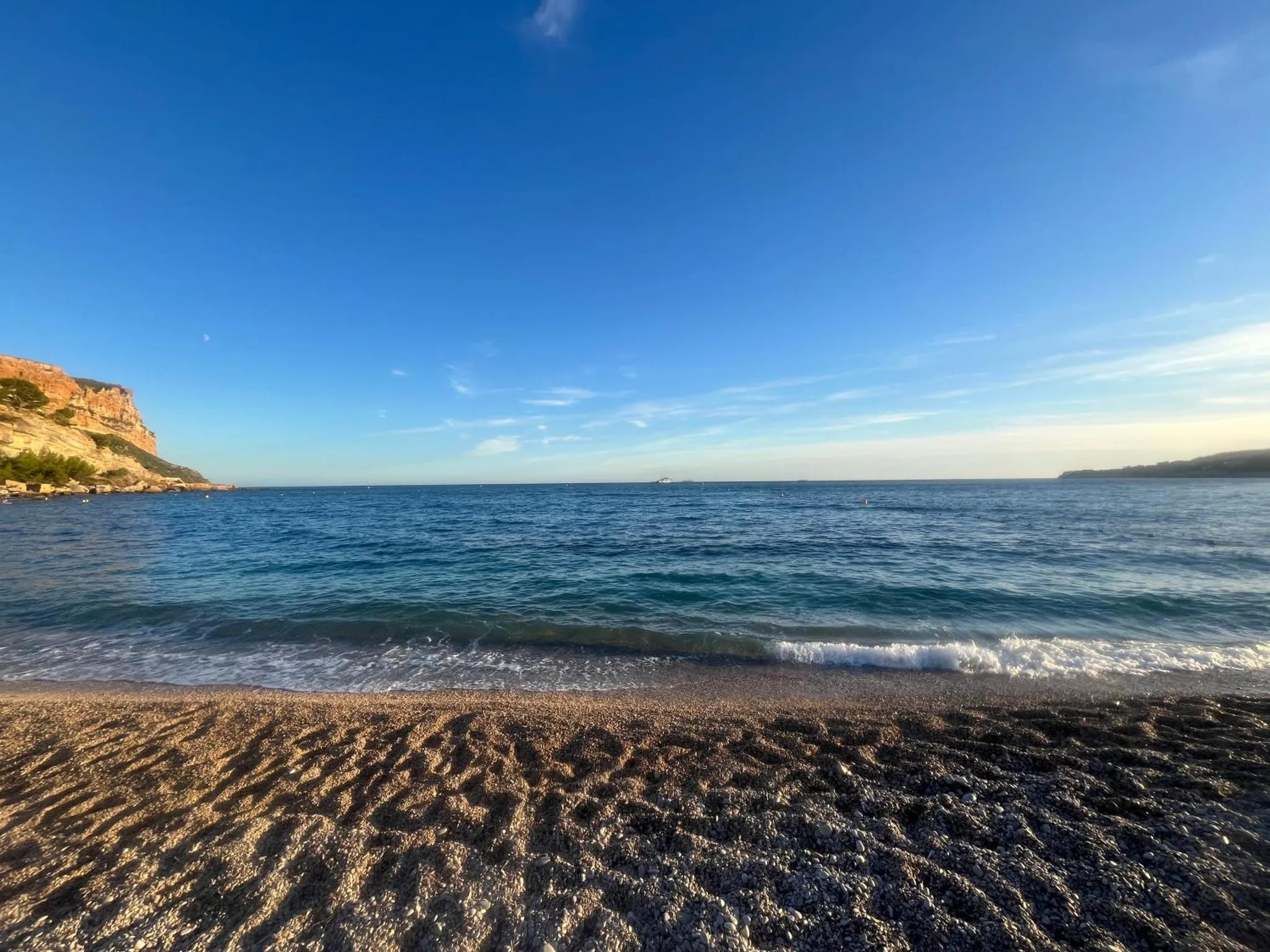 Une plage de galets borde une mer calme sous un ciel bleu.