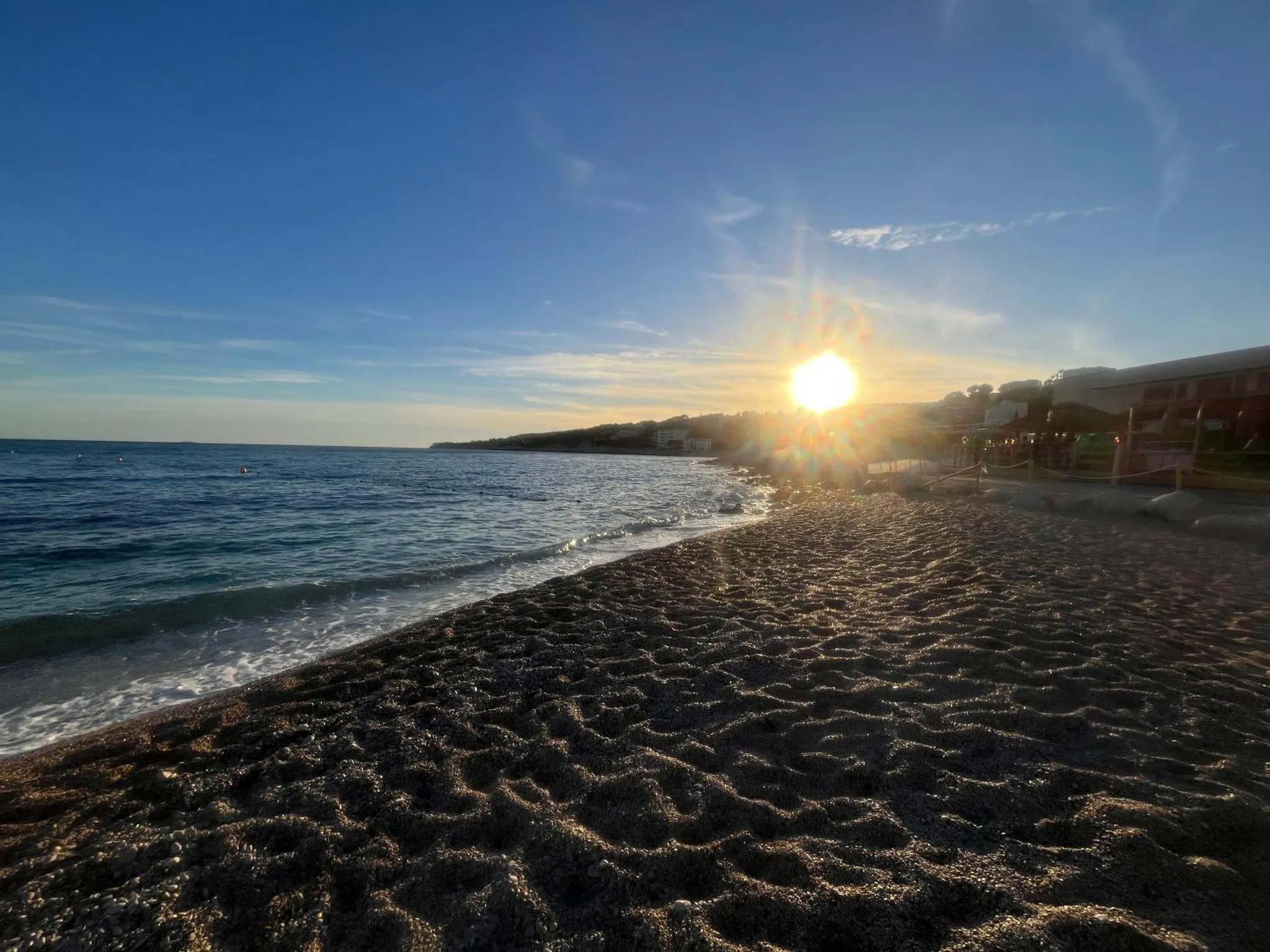 Plage de sable sombre avec vagues et soleil couchant sur la mer.