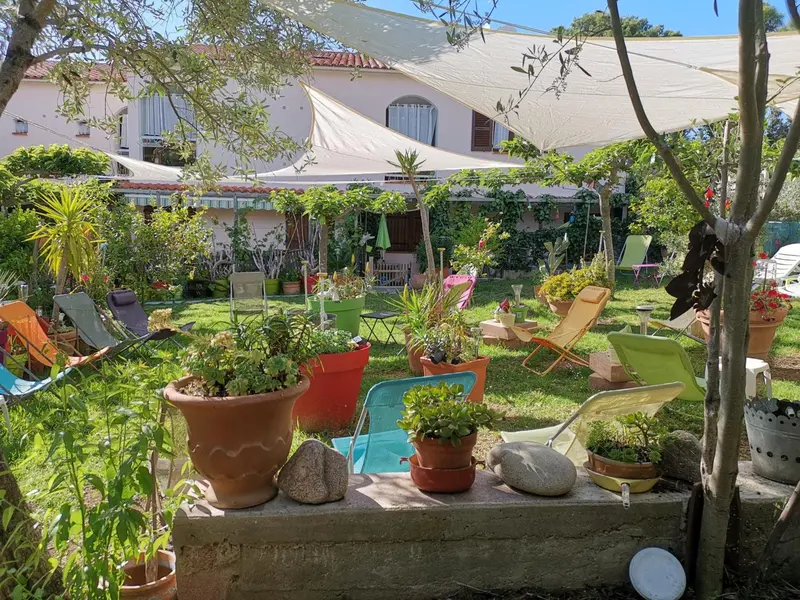 Un jardin verdoyant avec des transats et des pots de fleurs colorés devant un bâtiment.
