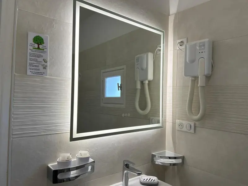 Une salle de bain moderne avec un grand miroir lumineux et des sèche-cheveux muraux.