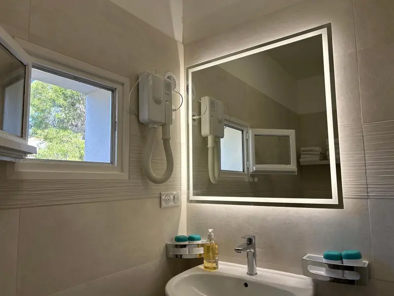 Une salle de bain lumineuse avec un grand miroir et un lavabo.