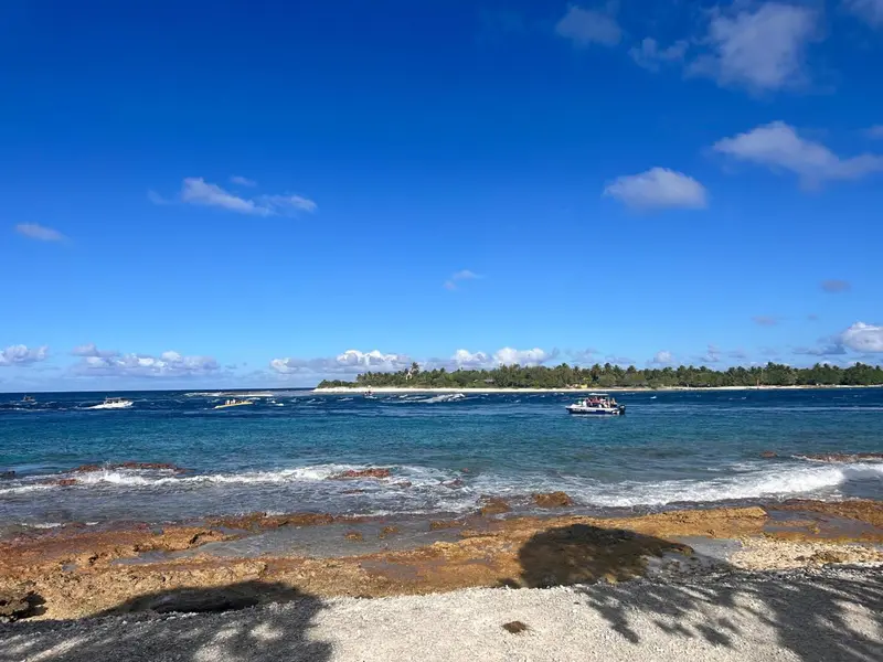 Une plage de sable clair borde une eau turquoise sous un ciel bleu nuageux.
