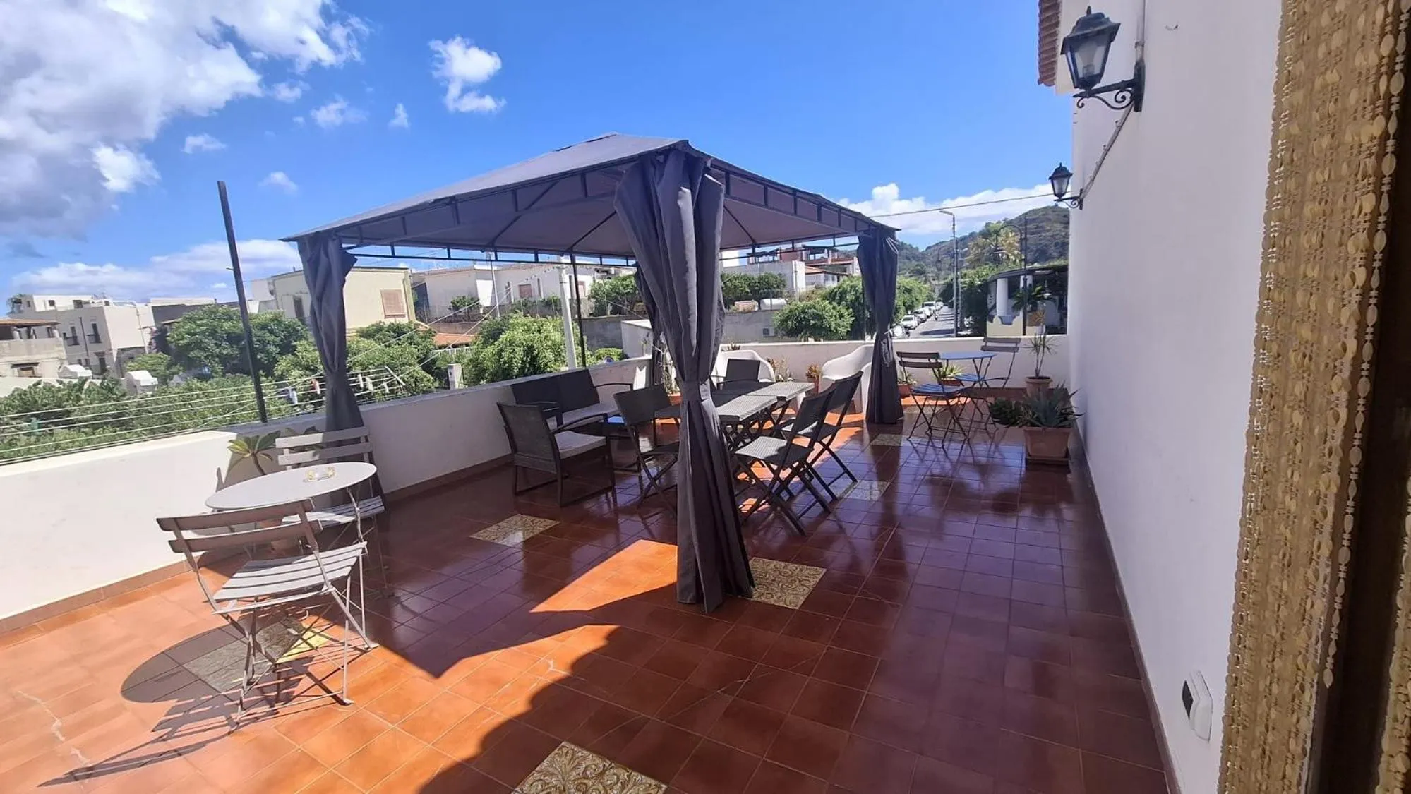 Terrasse ombragée avec tables et chaises donnant sur un paysage urbain et montagneux.