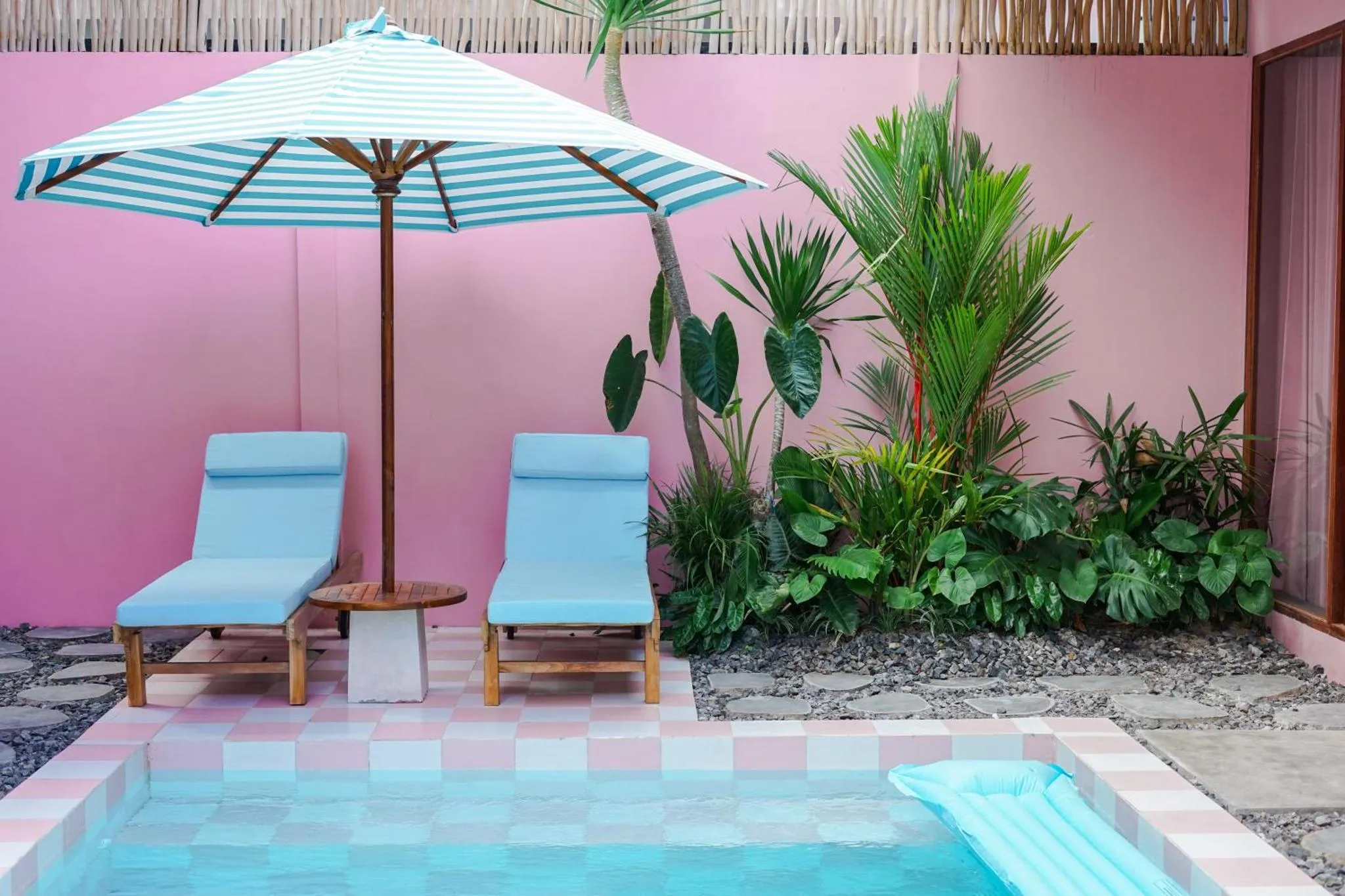 Deux transats bleus sont placés devant un mur rose et une petite piscine.