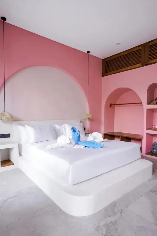 Une chambre lumineuse avec un grand lit recouvert de linge blanc et de quelques vêtements bleus.