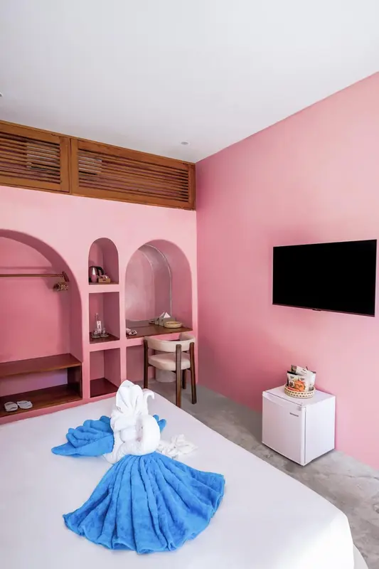Une chambre lumineuse aux murs roses avec un lit décoré de serviettes.