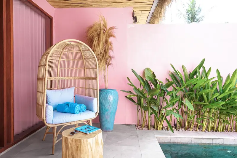 Un fauteuil suspendu en osier bleu se trouve sur une terrasse avec des plantes vertes.