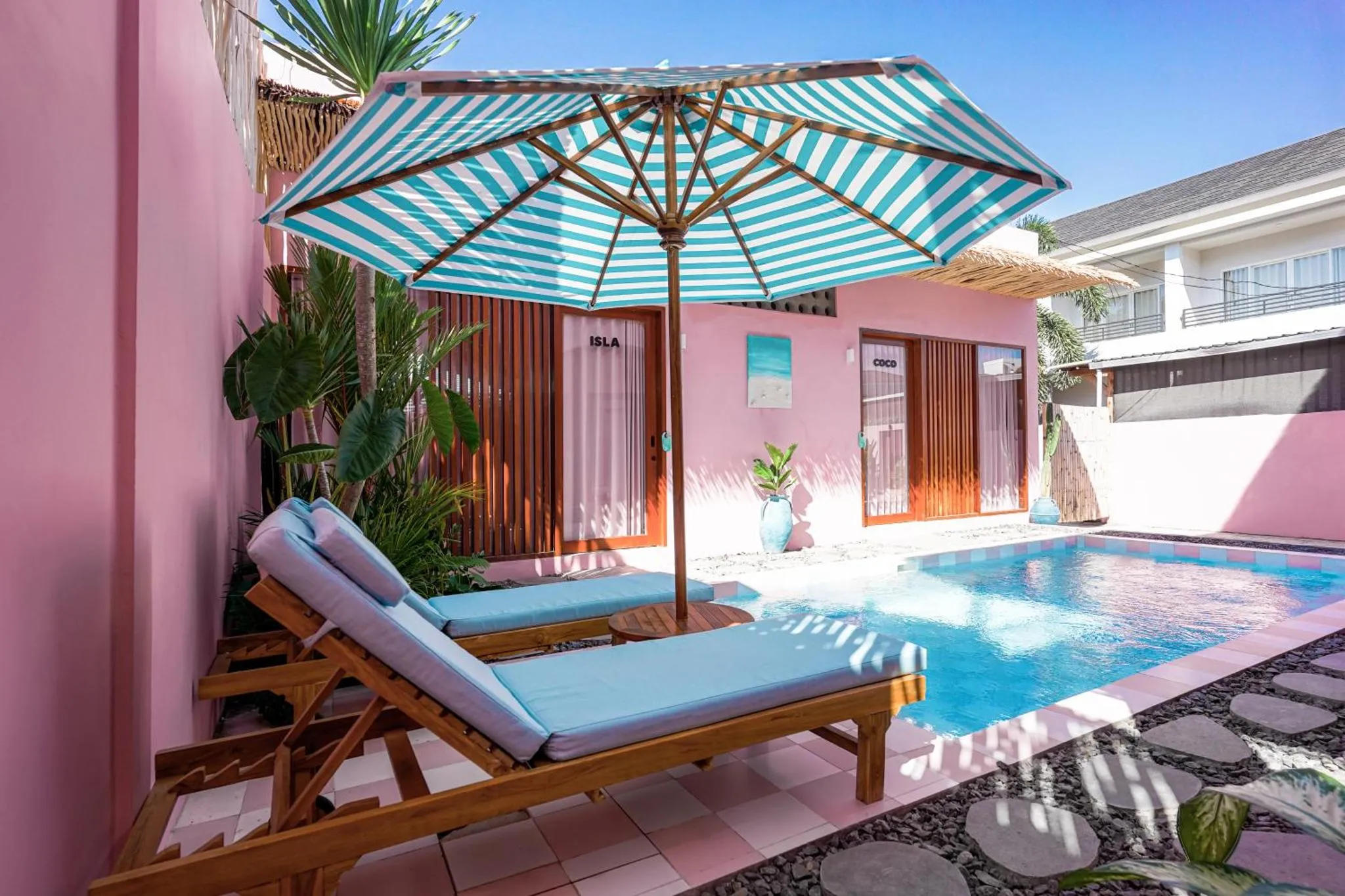 Transats bleus et parasol rayé au bord d'une piscine turquoise.