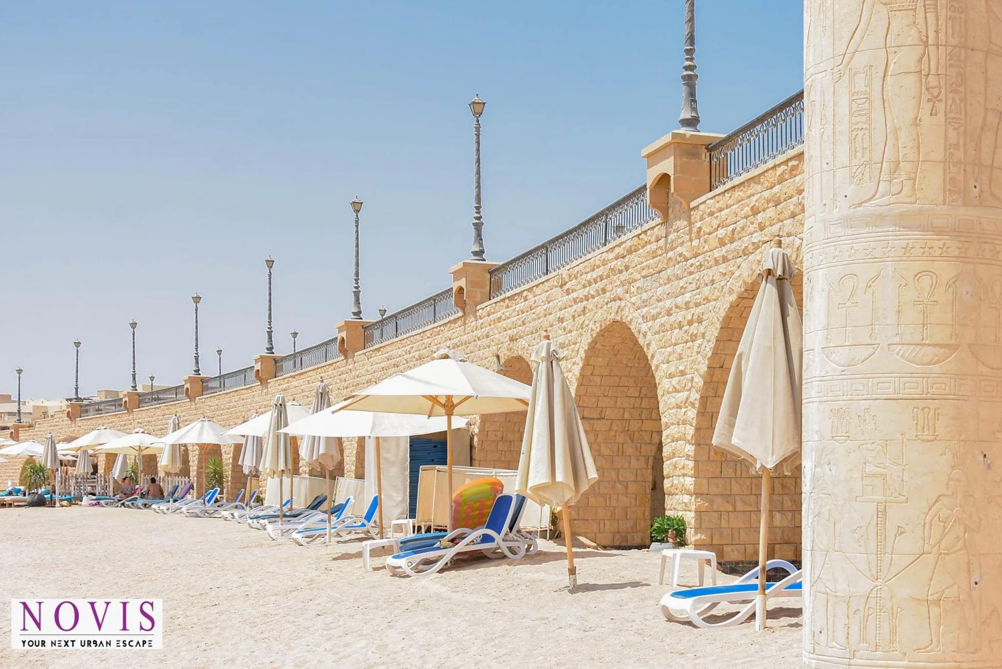 Terrasse en pierre avec parasols et transats sur une plage de sable.