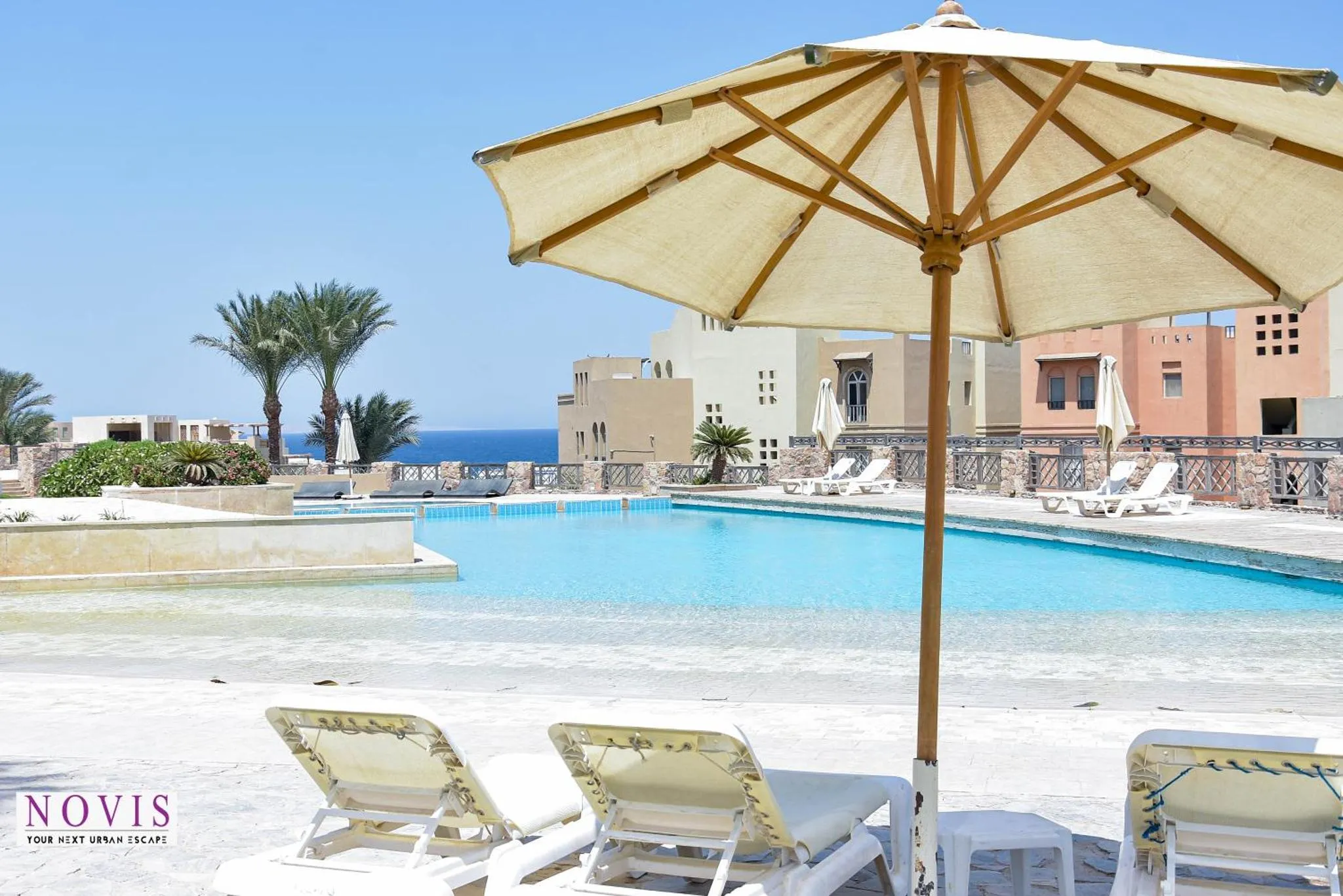 Transats blancs disposés devant une piscine turquoise et un bâtiment beige.