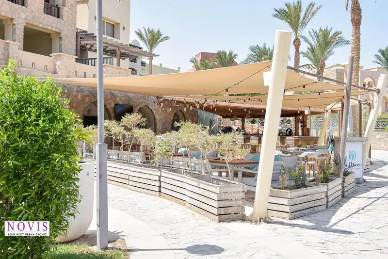 Terrasse ombragée avec tables et chaises près d'une végétation soignée.