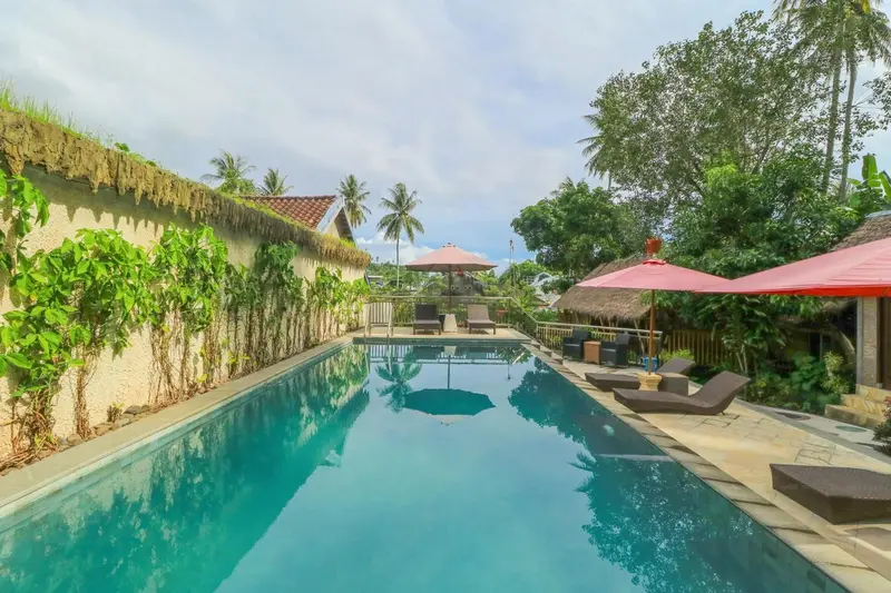 Une piscine rectangulaire bordée de chaises longues et de végétation luxuriante.