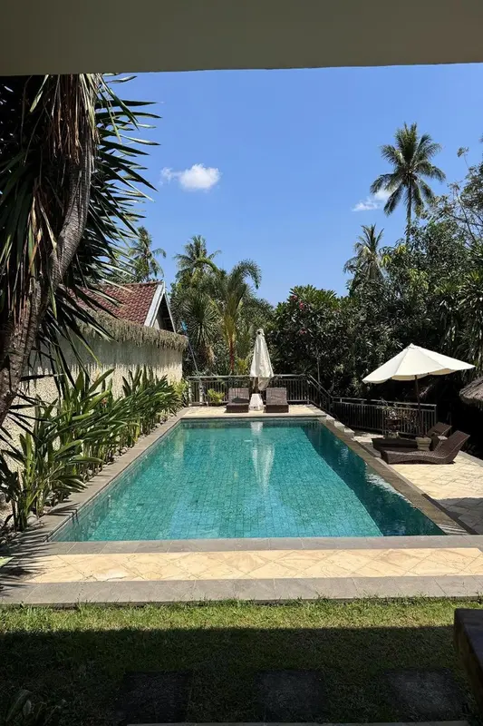 Une piscine turquoise bordée de transats et de végétation luxuriante sous un ciel bleu.