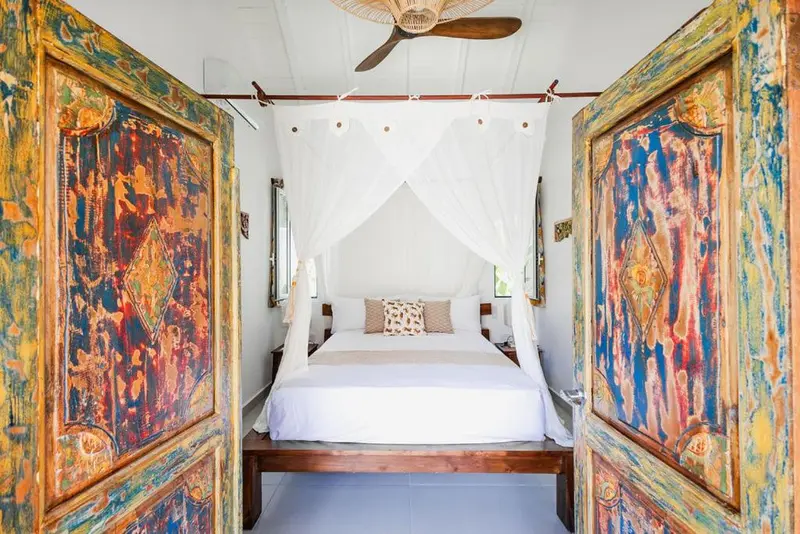 Une chambre lumineuse avec un lit à baldaquin et des portes colorées ouvertes.
