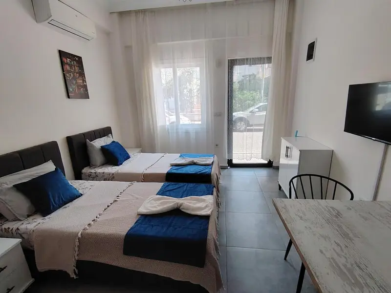Une chambre lumineuse avec deux lits et un bureau près d'une porte-fenêtre.