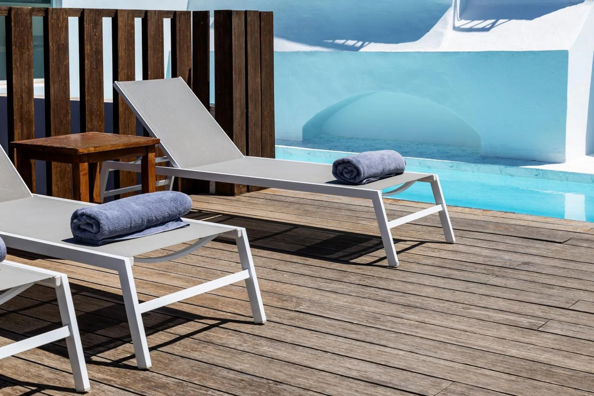 Transats et petite table basse sur une terrasse en bois près d'une piscine.
