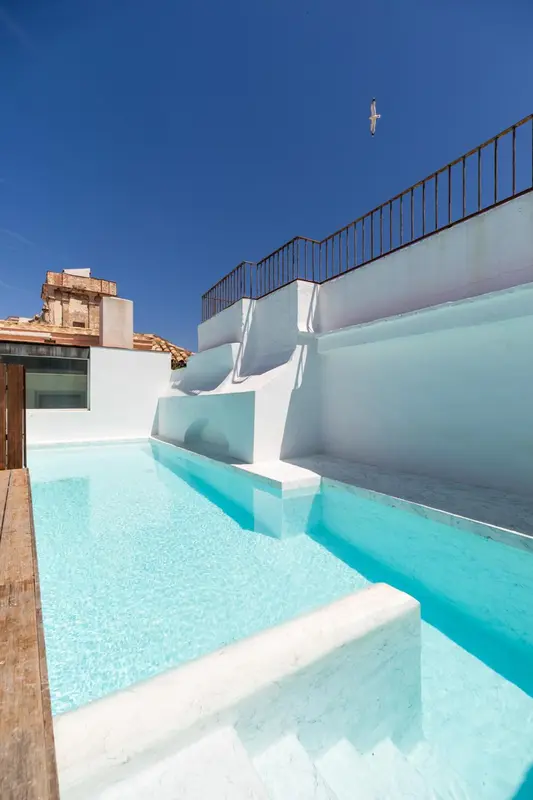 Piscine rectangulaire sur un toit-terrasse blanc avec escaliers intégrés.