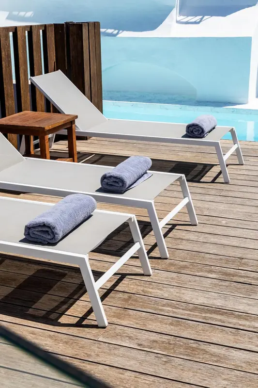 Transats blancs et serviettes enroulées au bord d'une piscine.