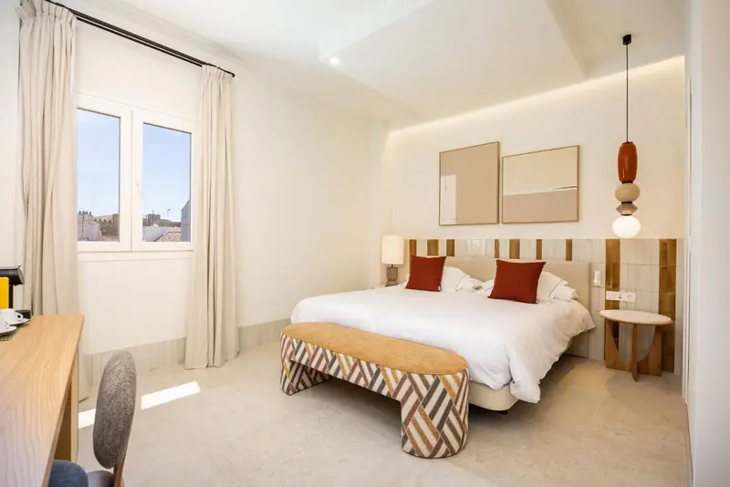 Chambre lumineuse avec un grand lit et une fenêtre donnant sur la ville.