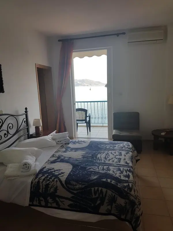 Une chambre lumineuse avec un lit fait et une vue sur la mer par une porte-fenêtre.