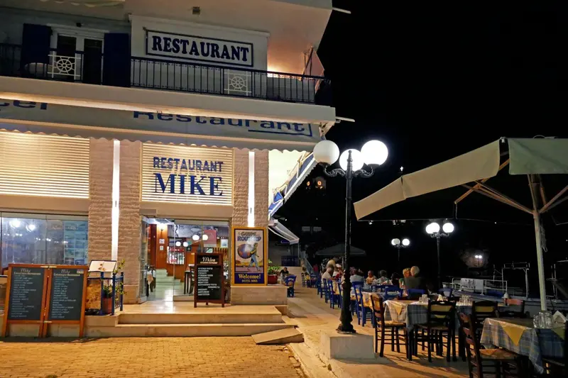 Façade d'un restaurant illuminé la nuit avec des tables en terrasse.