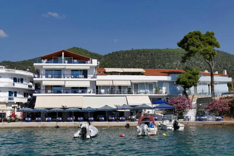 Bâtiment blanc avec des balcons donnant sur la mer et des bateaux amarrés au premier plan.