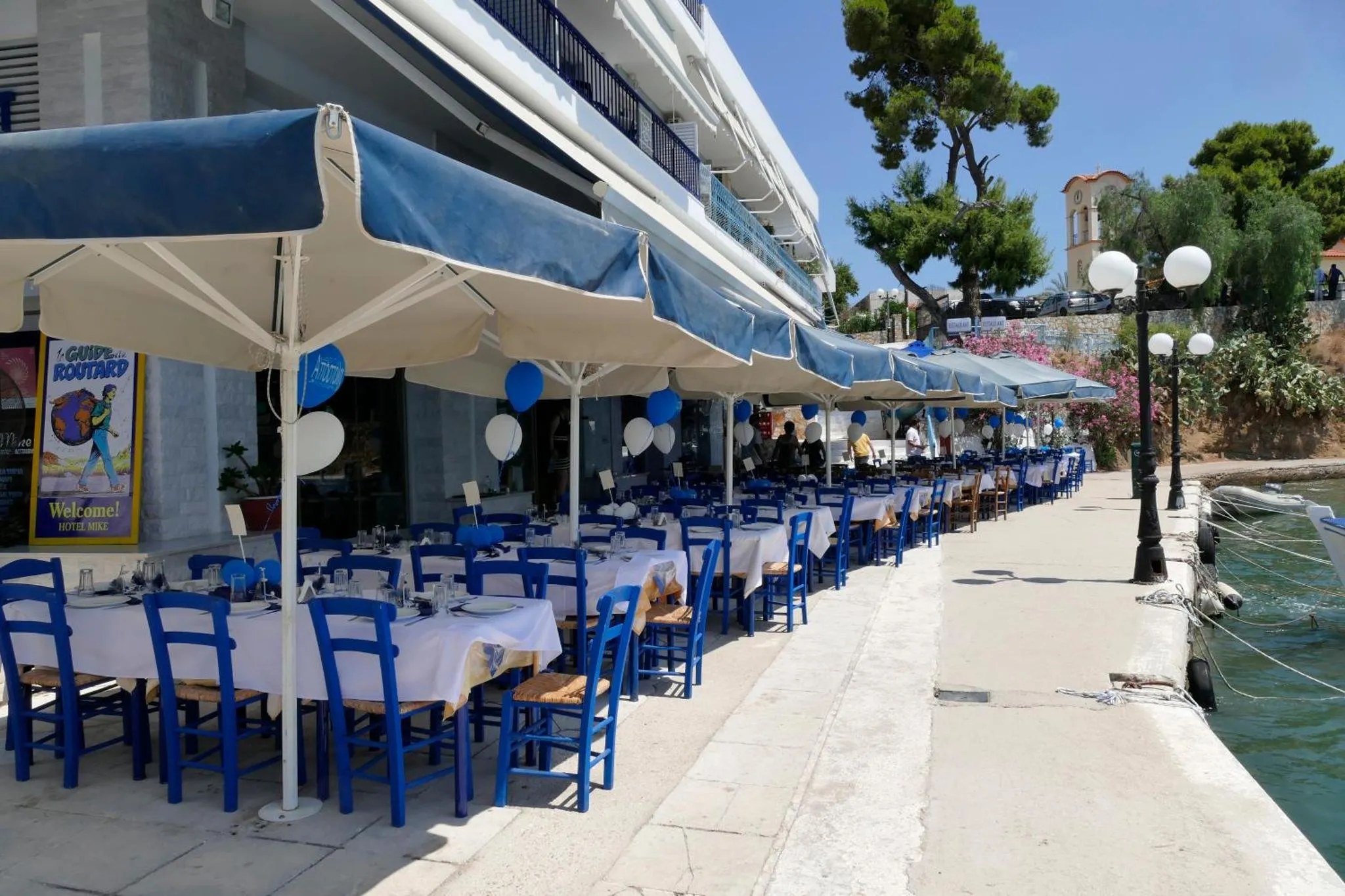 Terrasse ombragée avec tables et chaises bleues en bord de mer.