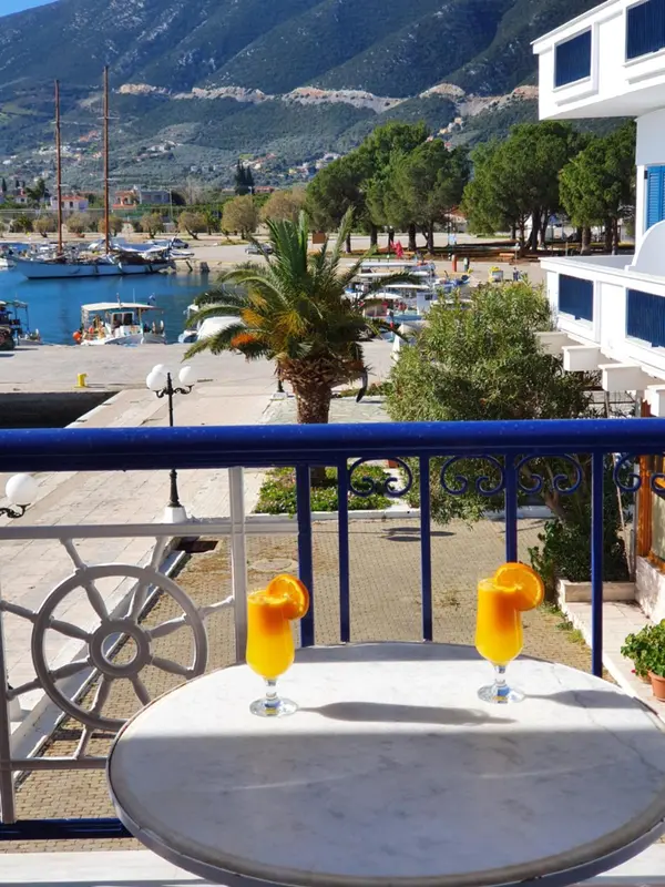 Une table avec des boissons est posée sur un balcon ensoleillé avec vue sur un port de plaisance.