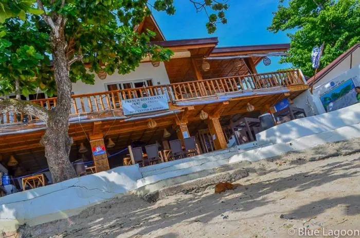 Bâtiment en bois sur pilotis avec une terrasse et des tables de restaurant en bord de mer.
