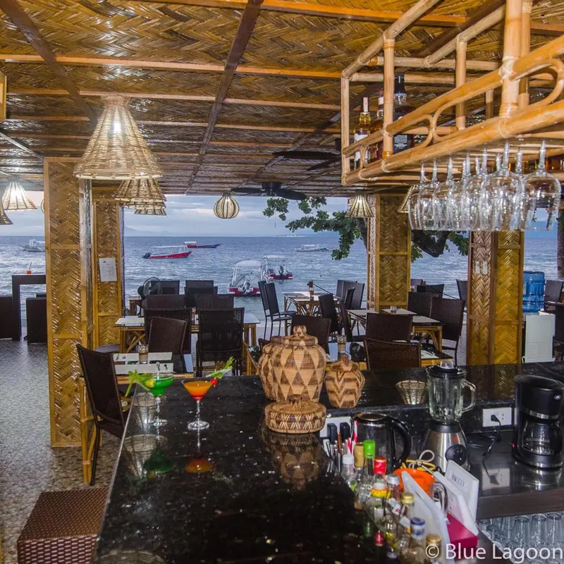 Un comptoir de bar en bois donne sur une salle à manger ouverte avec vue sur la mer.