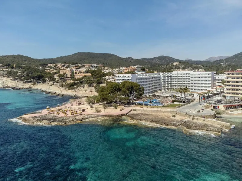 Vue aérienne d'un complexe hôtelier en bord de mer avec une plage et des collines en arrière-plan.